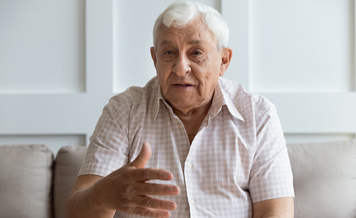 An older man sitting on a couch and speaking