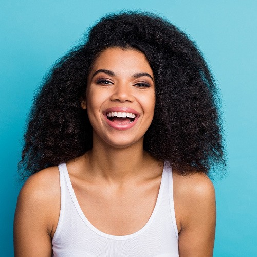 Woman in white tanktop smiling in front of light blue background