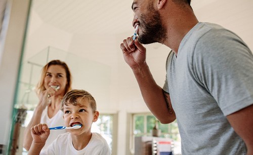 Woman, little boy, and man brushing teeth together