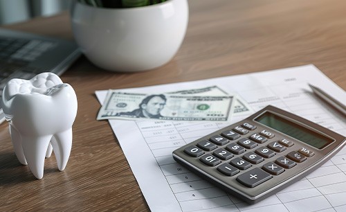 Model tooth on a desk next to calculator and dollar bills