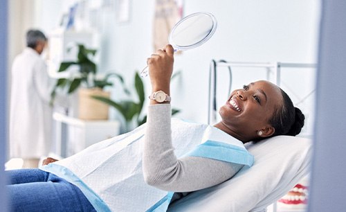 Woman smiling at reflection in handheld mirror