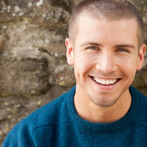 Man in blue shirt standing in front of stone wall