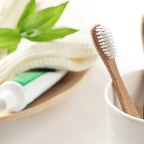 Two toothbrushes in a cup, toothpaste tube under a towel