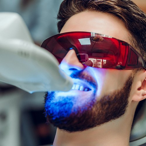 Man sitting in dental chair receiving teeth whitening