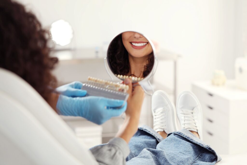 Woman looking in hand mirror as dentist holds shade guide to her teeth